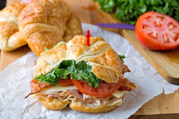 a sandwich with meat, lettuce and tomato on it sitting on wax paper