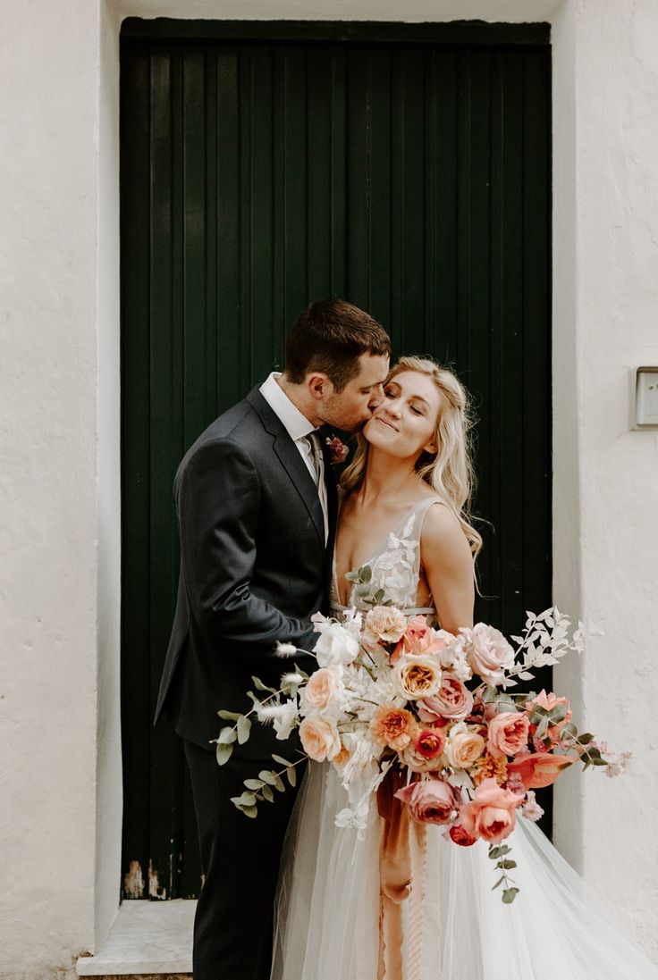 a bride and groom kissing in front of a green door with flowers on the floor