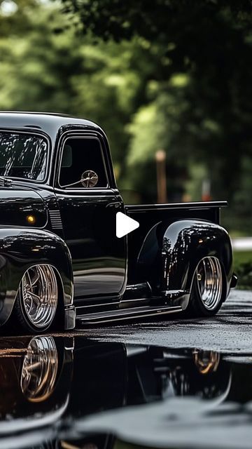 an old black pickup truck parked on the side of a road next to a puddle