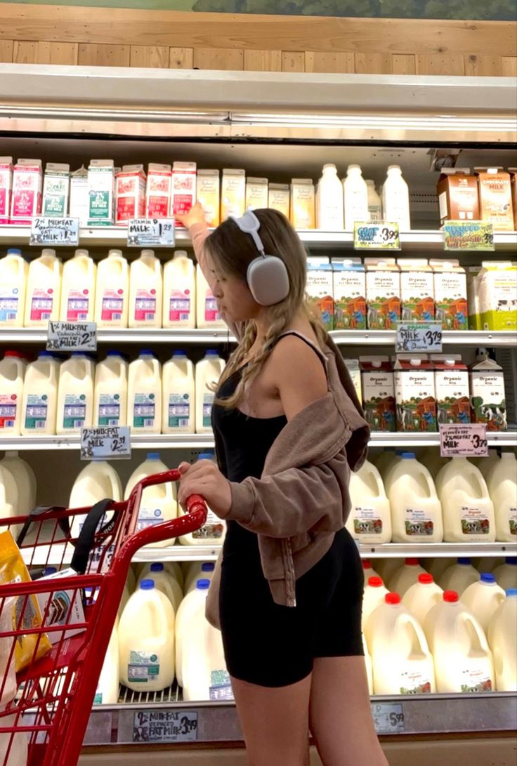 a woman with headphones standing next to a grocery cart in front of milk bottles