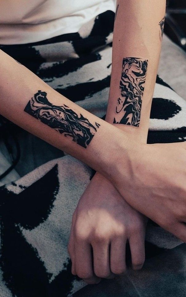 two people with tattoos on their arms sitting next to each other and holding hands together