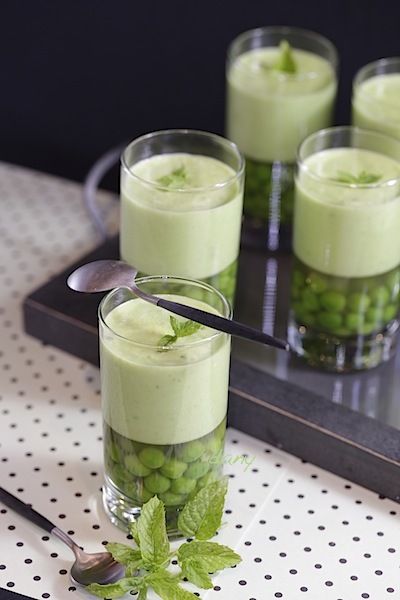 four glasses filled with green pudding on top of a black tray next to spoons