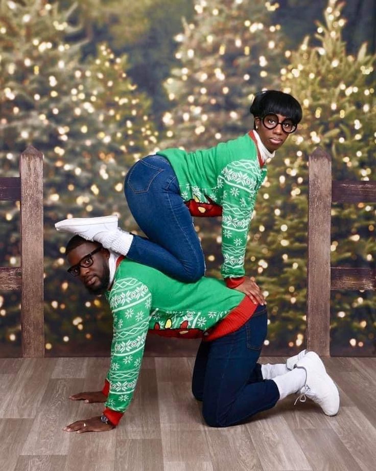 two people in matching outfits are posing for a photo with christmas tree lights behind them