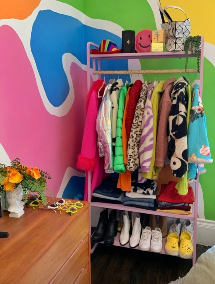 a rack with clothes and shoes on it in front of a colorful wall