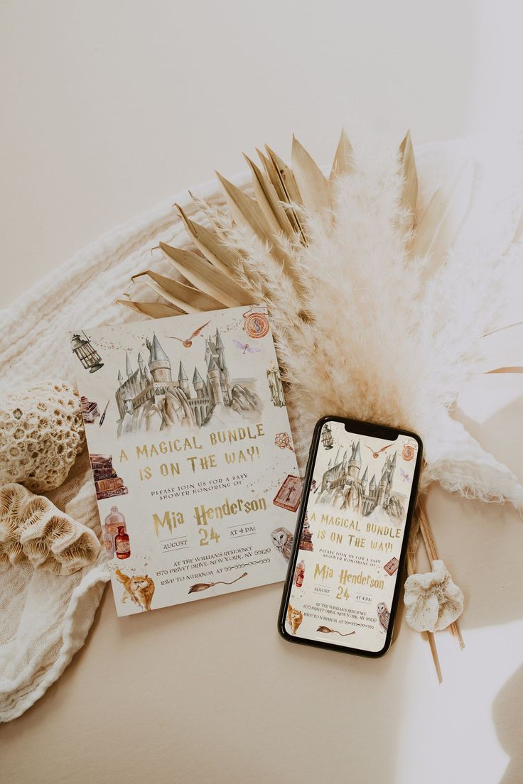 an open book next to a cell phone on a white surface with some feathers around it