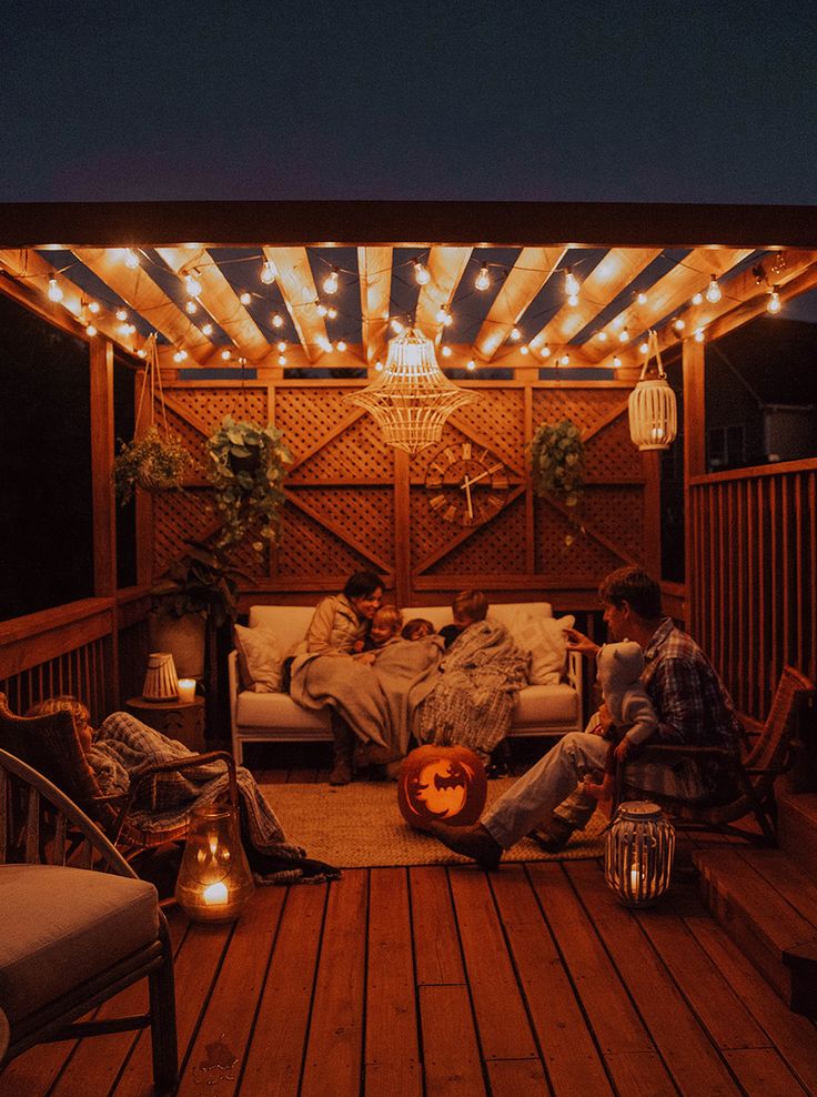 three people sitting on a porch with lights strung over the roof and in the background