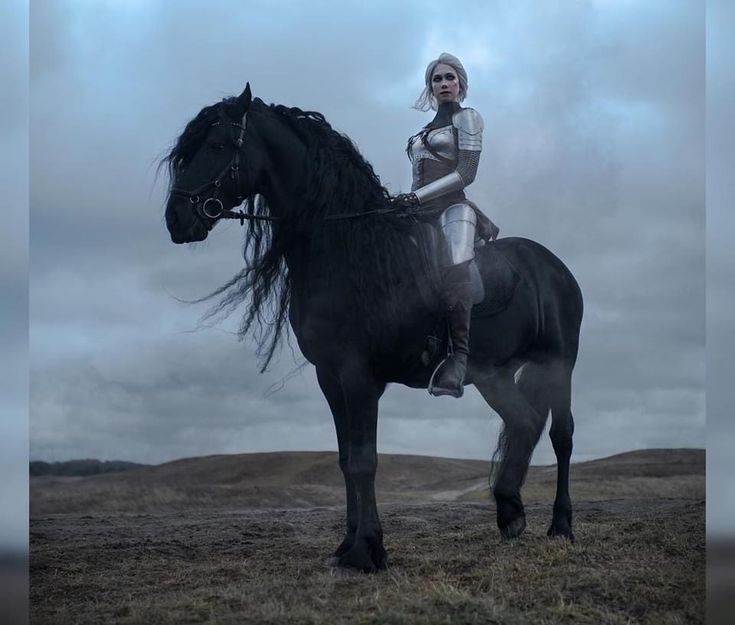 a woman riding on the back of a black horse in an open field under cloudy skies