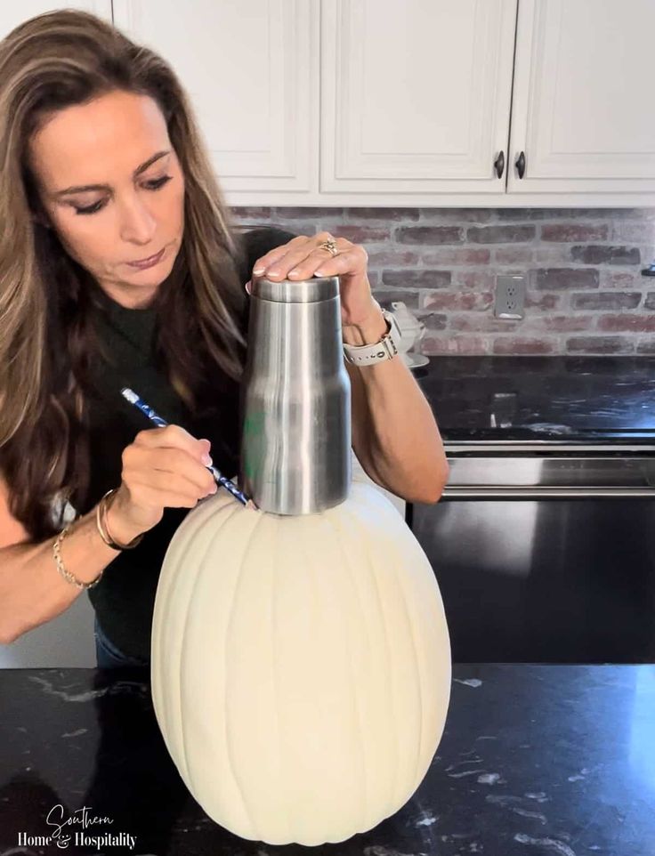 a woman is decorating a white pumpkin on the kitchen counter top with a marker