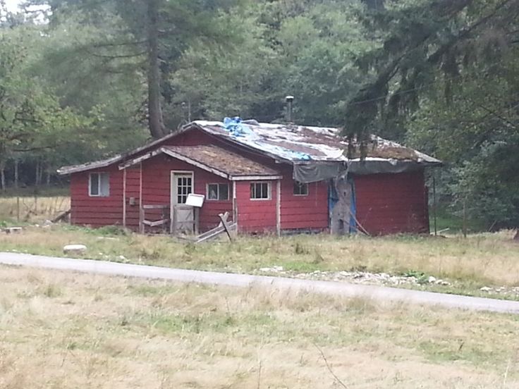 an old red house in the middle of a field with trees and grass around it