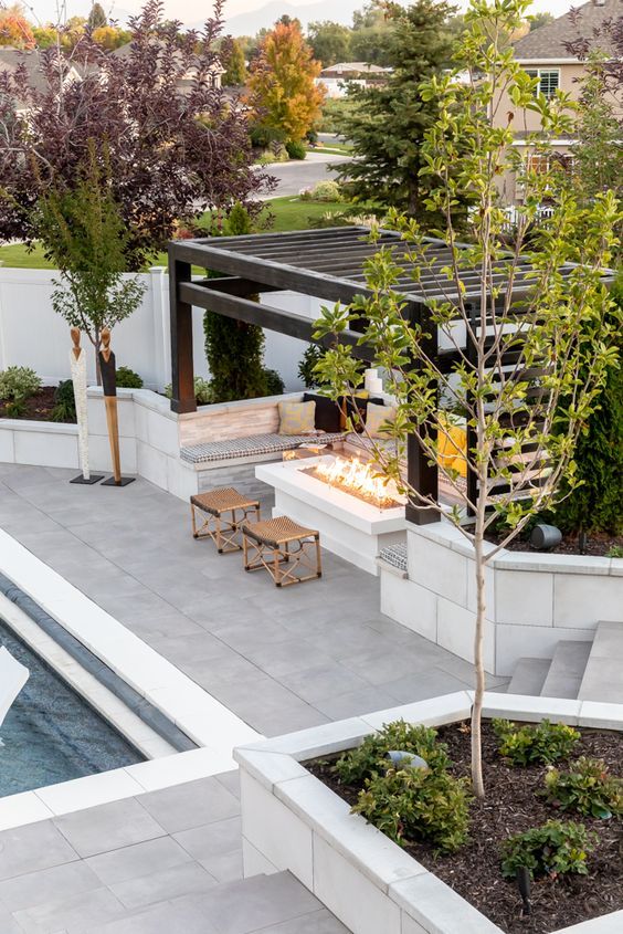 an outdoor fire pit surrounded by trees and landscaping area with benches, tables and chairs