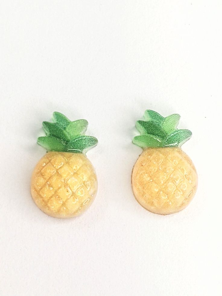 two yellow pineapples with green leaves sitting on top of each other in front of a white background