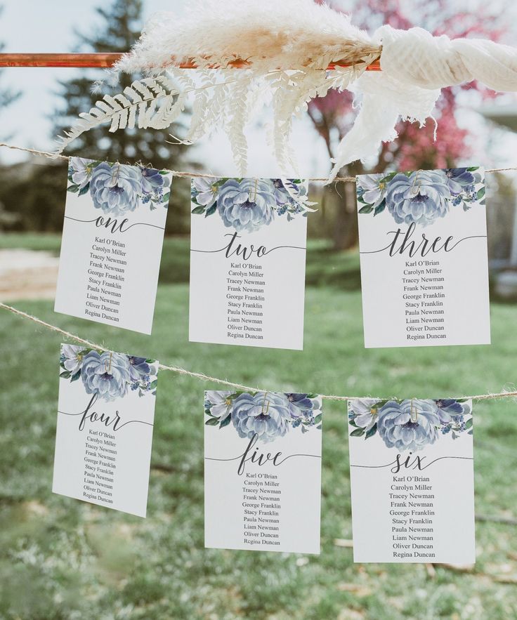 wedding seating cards hanging from a line in the grass with flowers and feathers on them