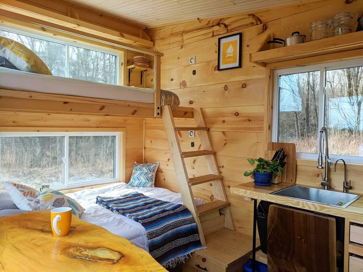 a kitchen and bedroom in a tiny cabin with wooden walls, wood flooring and ladder to the ceiling