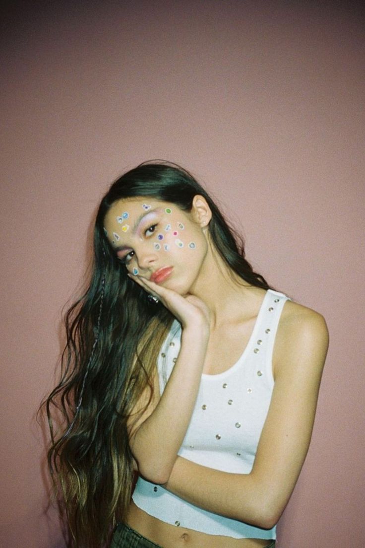 a woman with makeup on her face and long hair posing in front of a pink wall