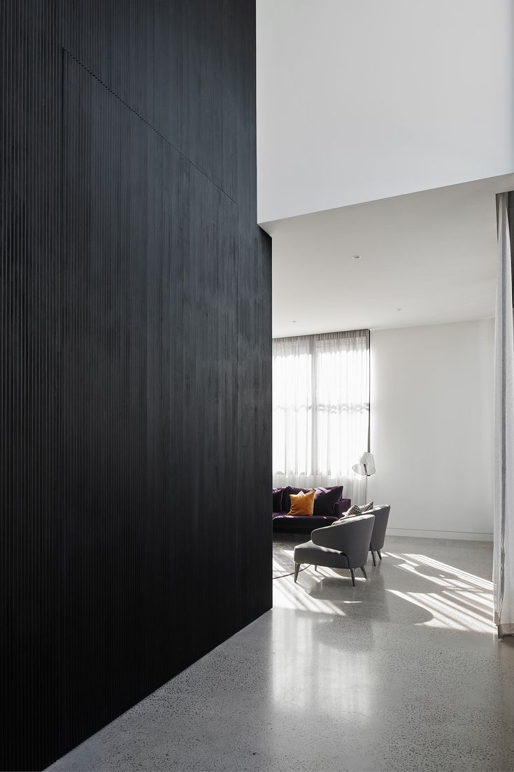 an open living room with black walls and white flooring is seen from the hallway