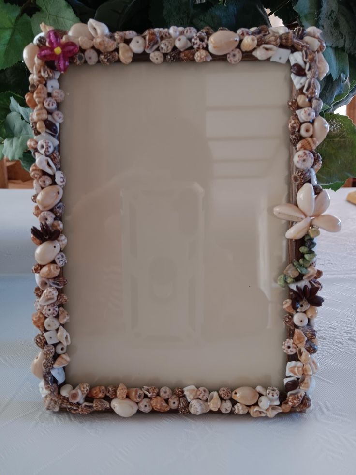 there is a frame made out of seashells on the table with flowers in the background