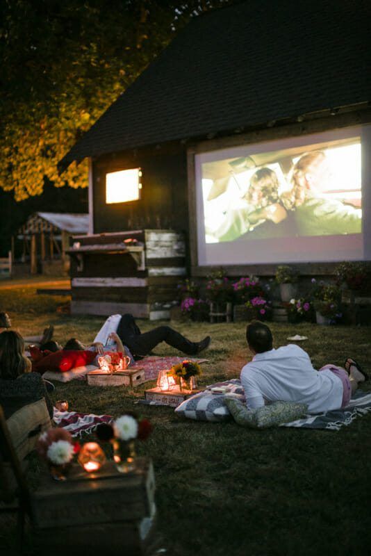 people sitting on the grass watching movies in front of a movie screen at night time