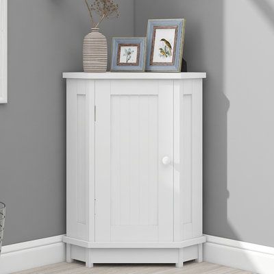 a white cabinet with two pictures on top and a vase next to it in the corner