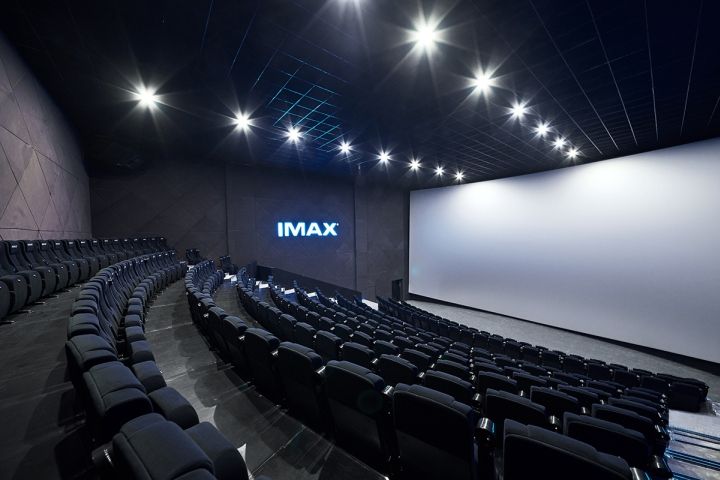 an empty auditorium with rows of seats and projection screen in the center, showing imax's logo