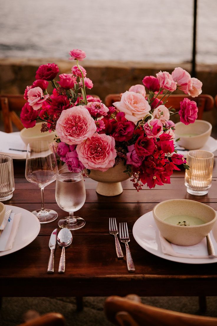 the table is set with pink flowers and silverware, along with plates and utensils