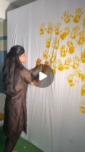 a woman standing in front of a wall with yellow hand prints on it