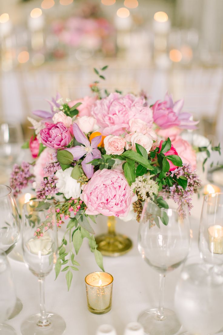 a vase filled with pink and white flowers sitting on top of a table next to wine glasses