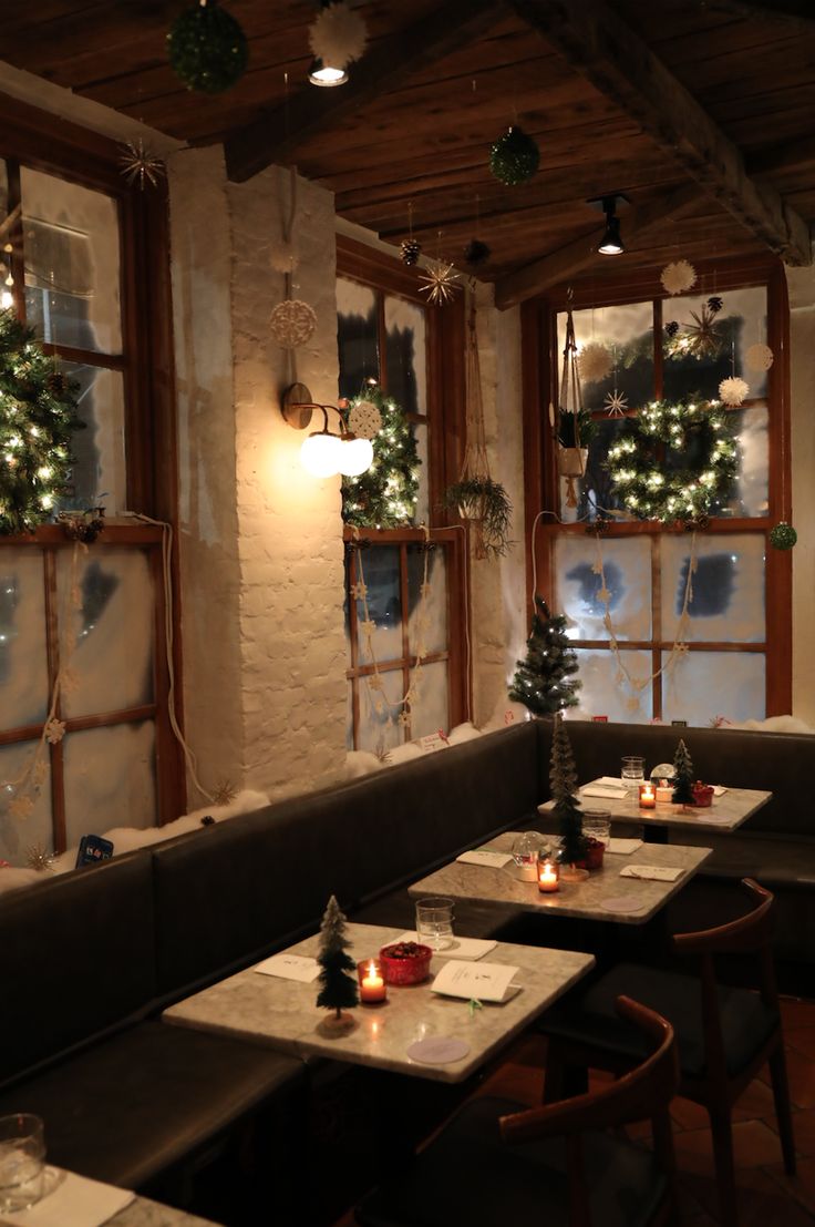 an empty restaurant with christmas decorations on the windows and tables in front of them, lit by candles