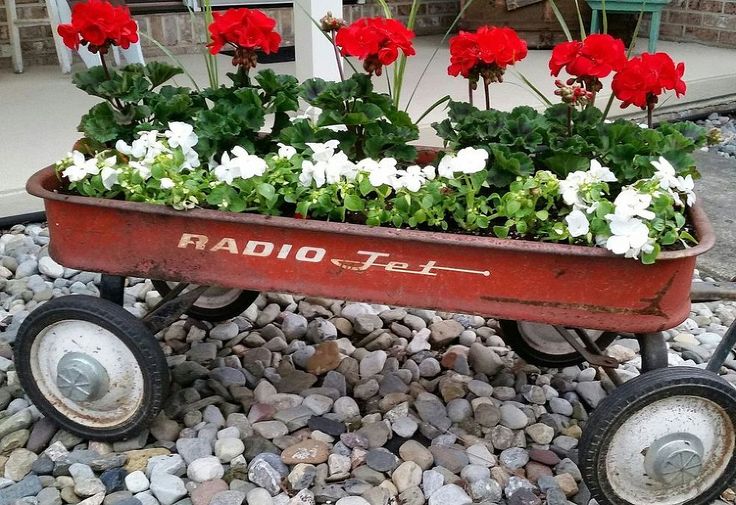 a red wagon filled with flowers sitting on top of a pile of rocks and gravel