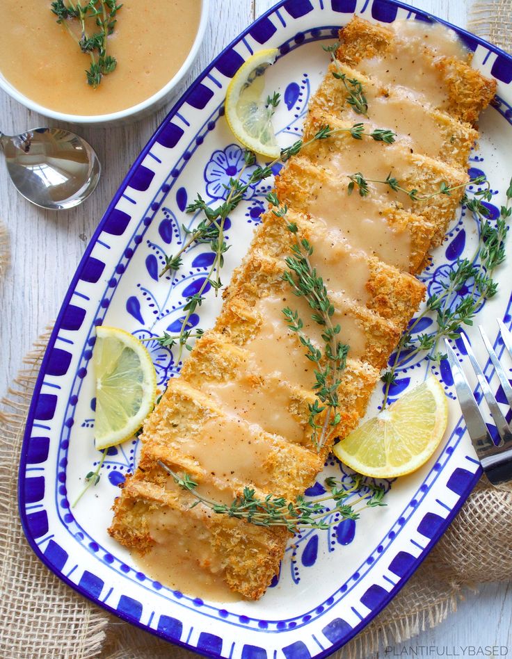 fish fillets on a blue and white plate with lemons, herbs and sauce