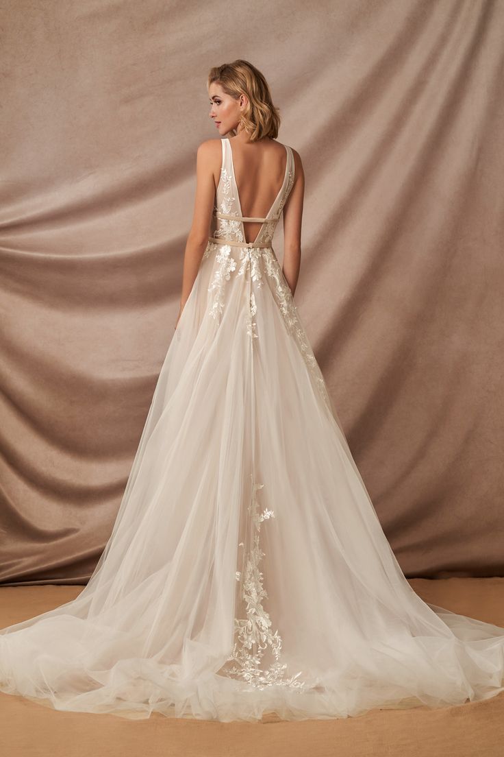 a woman in a wedding dress standing on a beige background with her back to the camera