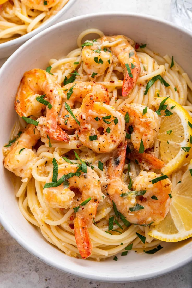 two bowls filled with pasta and shrimp, garnished with parsley on the side