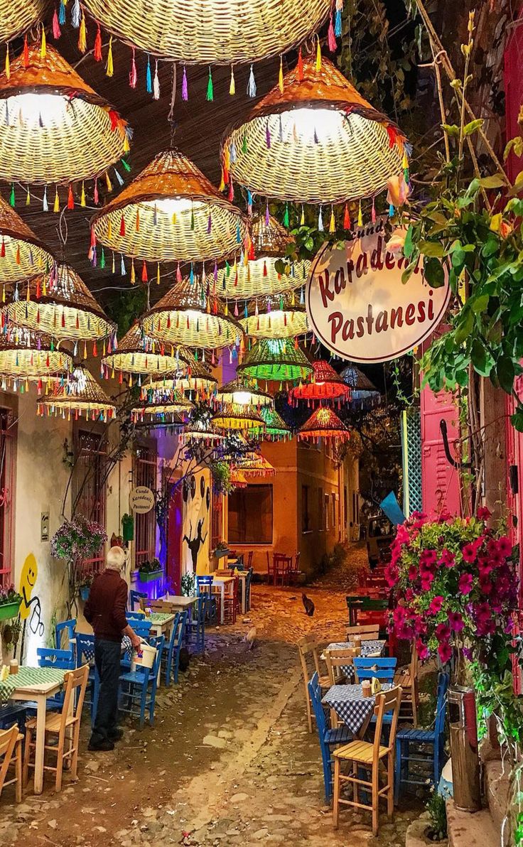 an outdoor restaurant with lots of lights hanging from the ceiling and tables covered in colorful umbrellas