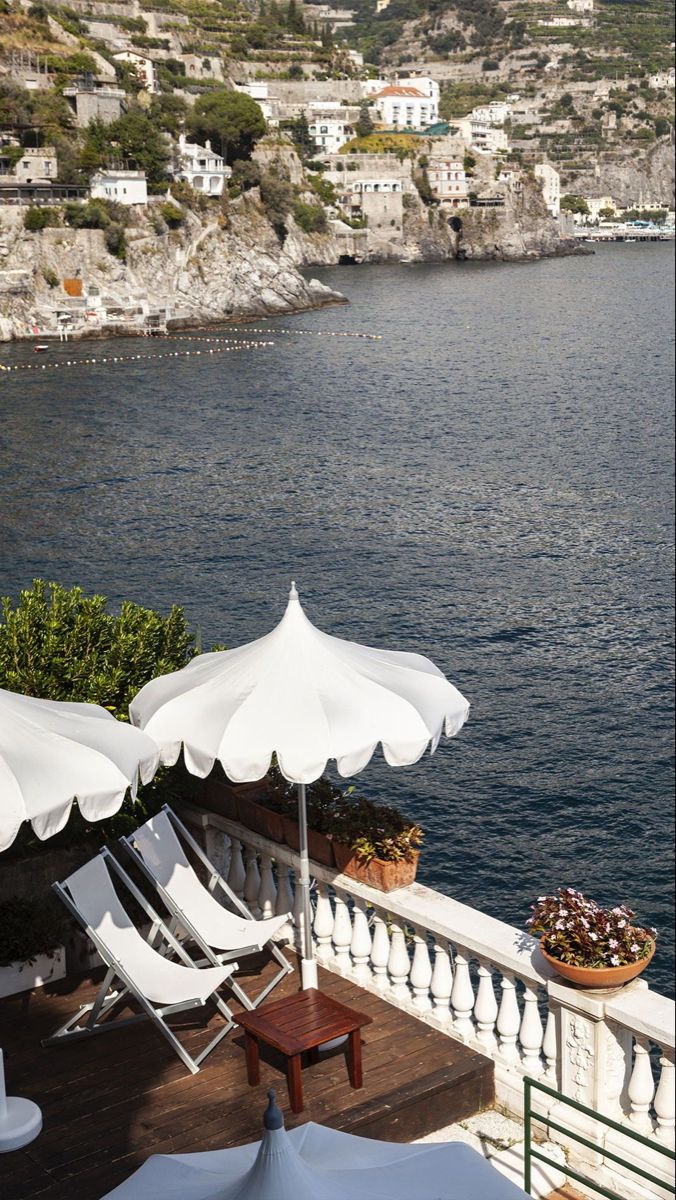 some chairs and umbrellas on a balcony overlooking the water