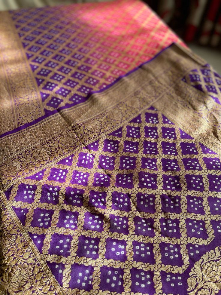 A Handmade Purple & Neon Coral Pink shaded Pure Khaddi Georgette Bandhani/ Bandhej Saree woven in pure Meenakari Zari- an invitation for a true self-indulgence. The fall and pico are done for this saree. It comes along with a Purple Bandhani Blouse piece that also has a zari border.   Our Policy on Returns, refunds and exchanges: We don't accept requests for returns and exchanges on the below observations: Non-defects: *Small knots or bumps in the silk threads.  *Uneven threads because of korvai Traditional Purple Pre-draped Saree For Navratri, Traditional Purple Pre-draped Saree For Puja, Traditional Wear With Zari Work In Purple For Festivals, Purple Pre-draped Saree With Cutdana For Traditional Ceremonies, Purple Traditional Wear With Zari Weaving For Festivals, Purple Cutdana Traditional Wear For Festivals, Purple Traditional Wear With Cutdana For Festivals, Purple Banarasi Silk Traditional Wear For Festivals, Traditional Gold Dupatta With Bandhani Print