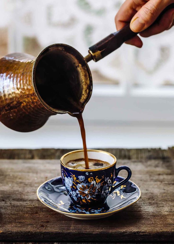 a person pours coffee into a blue and white cup on top of a wooden table