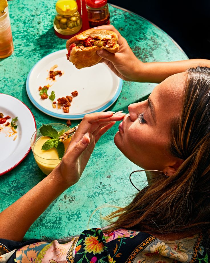 a woman sitting at a table with food and drinks in front of her, eating