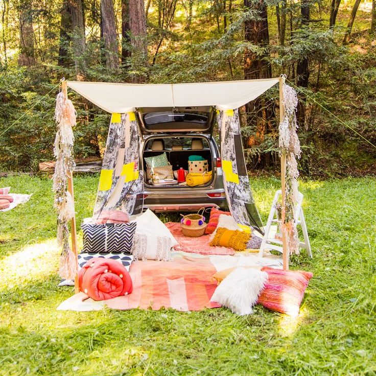 an outdoor picnic with food and drinks on the grass in front of a van parked in the woods