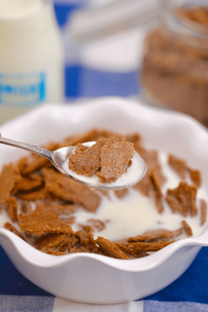 a spoon full of cereal and milk on a table with other foods in the background