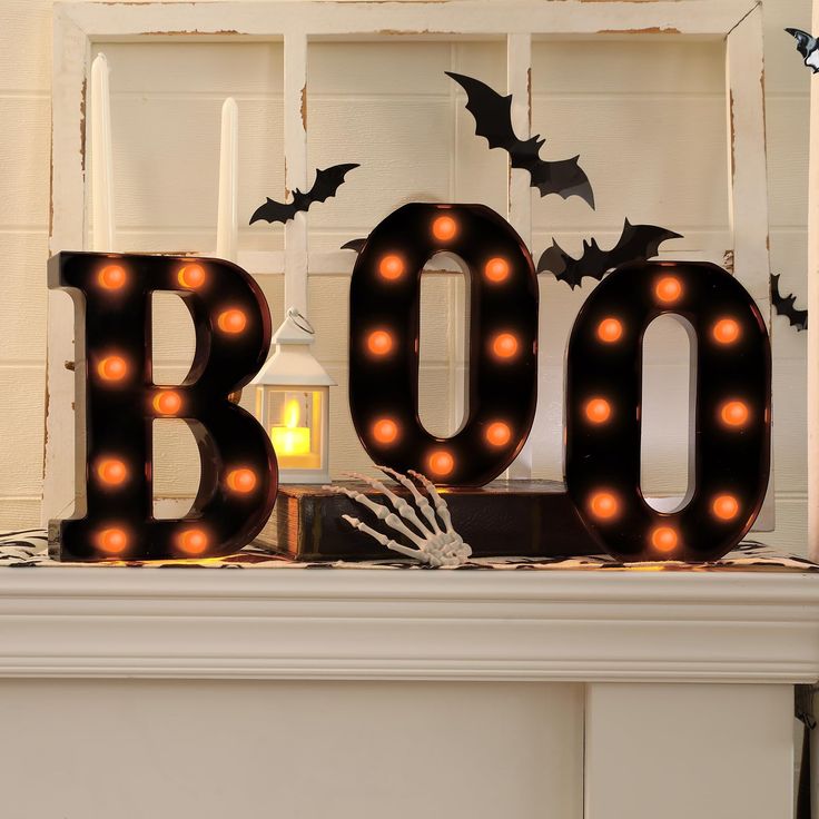 a lighted boo sign sitting on top of a mantle next to a candle and some bats