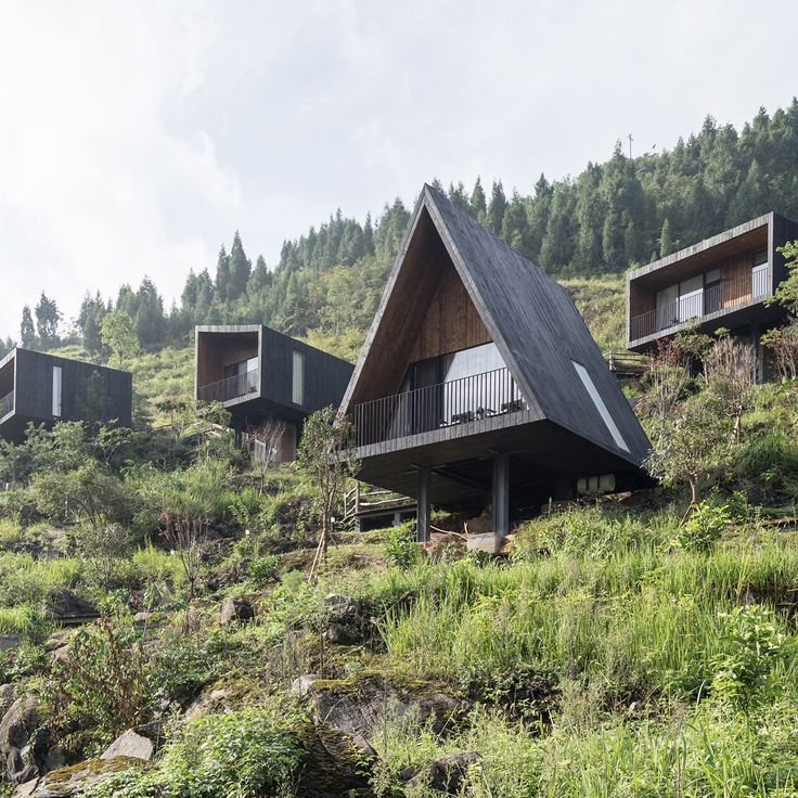 several cabins on the side of a hill with trees in the background and grass below