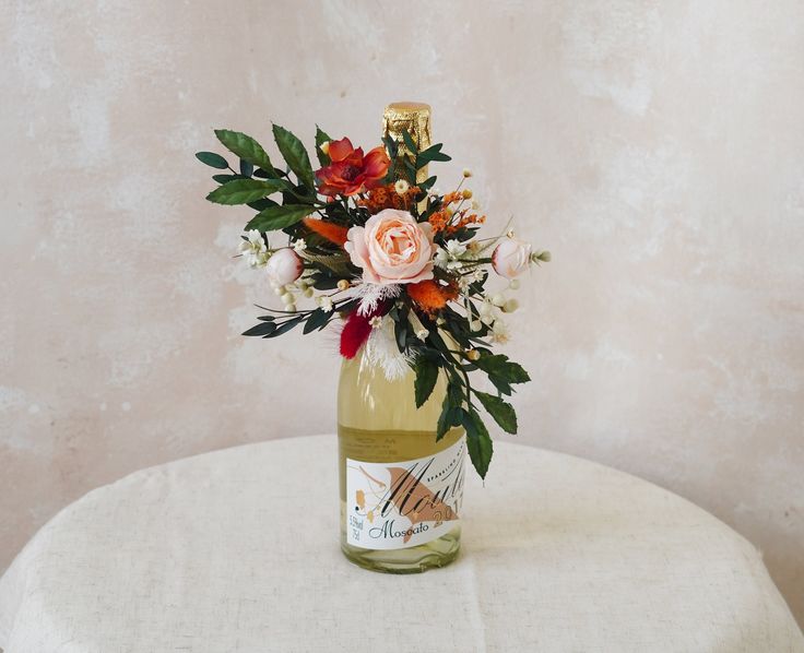 a bottle filled with flowers sitting on top of a white tablecloth covered round table