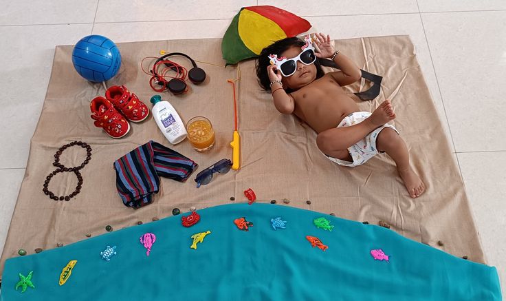 a little boy laying on top of a beach towel next to toys and other items