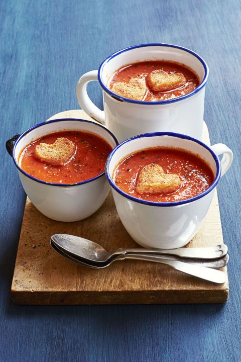 three bowls of soup with heart shaped bread on top and spoons next to them