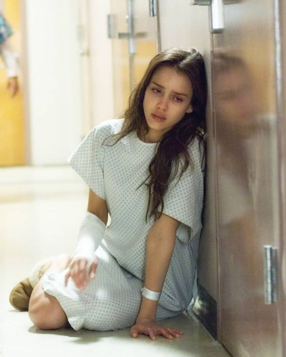 a young woman sitting on the floor next to a metal locker with her arm wrapped in bandages