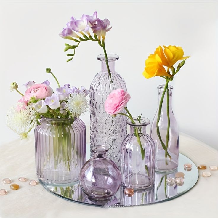 several vases with flowers in them sitting on a glass tableclothed surface,