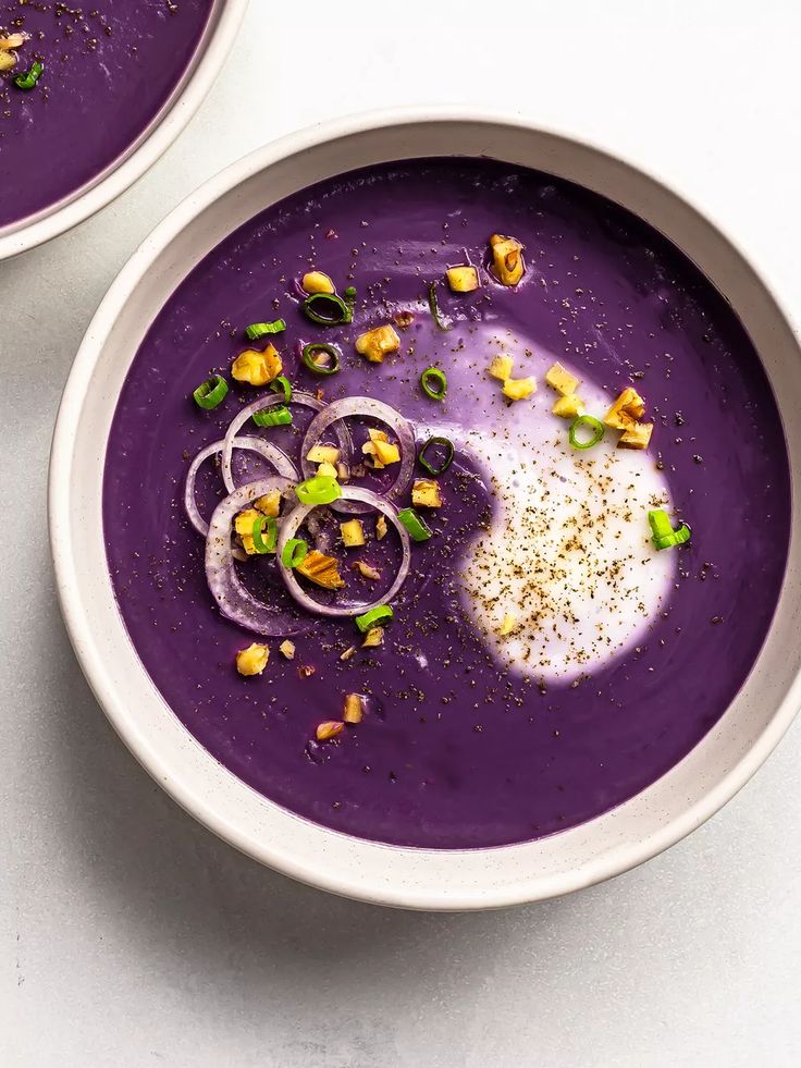 two white bowls filled with purple soup and garnished with chopped green onions on top