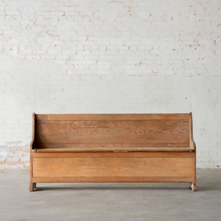 an old wooden bench sitting in front of a white brick wall with no one on it