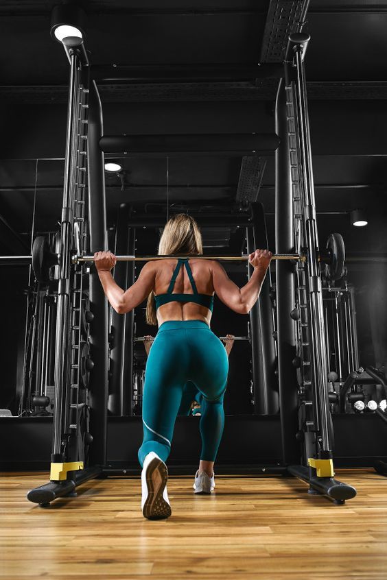 a woman is doing squats with a barbell in the middle of a gym