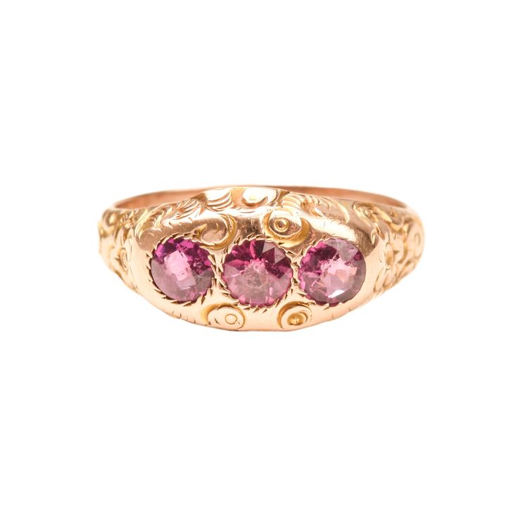 An incredible Victorian Etruscan 12K pink sapphire three-stone band ring. Features engraved floral and scroll motifs with three round-cut pink sapphires. The stones sit flush in round jagged settings and really pop against the gold band.  This ring has not been appraised but the stones are believed to be natural and remain in great condition with minimal surface wear. The gold facade has a polished finish with only minor tarnishing. There are no notable hallmarks or makers mark but the gold has Elegant Three Stone Pink Sapphire Jewelry, Elegant Pink Ruby Three Stone Ring, Pink Three Stone Ruby Ring, Elegant Pink Three-stone Ruby Ring, Fine Jewelry Pink Three Stone Jewelry, Pink Three-stone Sapphire Jewelry, Pink Sapphire Three-stone Jewelry, Pink Sapphire Three Stone Jewelry, Fine Pink Three Stone Jewelry