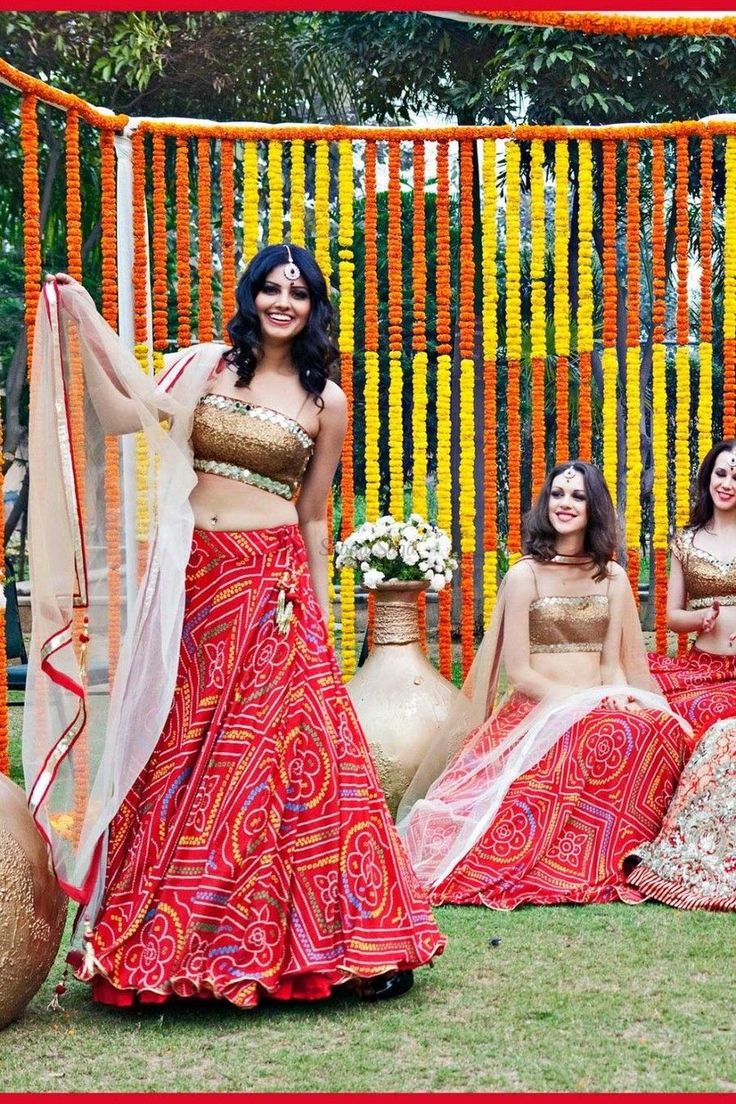 three women dressed in red and gold sitting on the grass with vases behind them